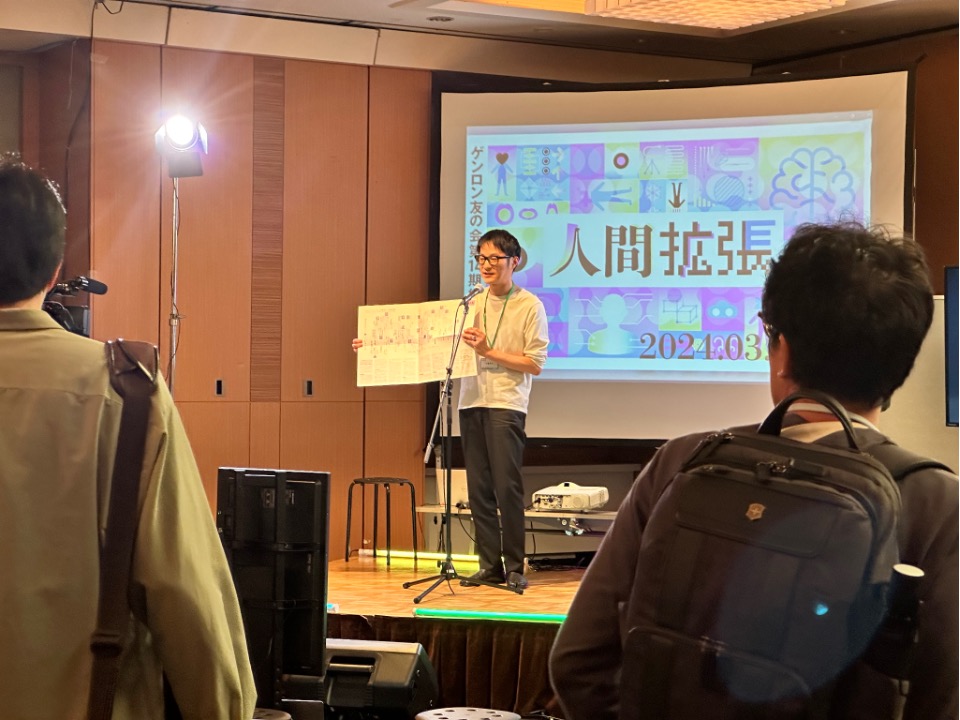 ステージで機関紙の紹介をする石橋の写真